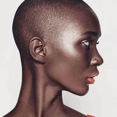 Side profile of a person with a shaved head wearing a red top against a white background