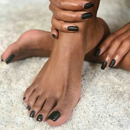 Close-up of feet with black nail polish on a light background