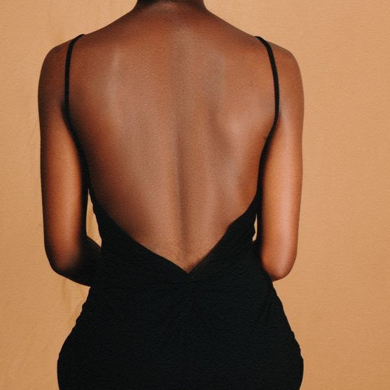 Woman wearing a black dress with a sheer back, standing against a beige background