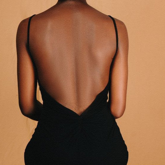 Woman wearing a black dress with a sheer back, standing against a beige background