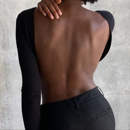 Person wearing a black long-sleeve top with a textured wall background