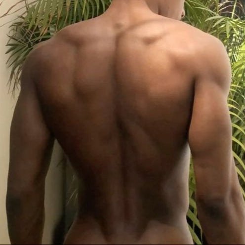 Man with a muscular back standing in front of green plants